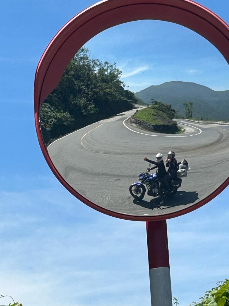 Mirror reflection of winding mountain road with motorbikers in Vietnam, showcasing scenic landscapes.