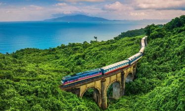 Vivid scene of a modern train crossing lush green hills with ocean view in the background, showcasin.