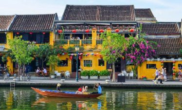 Hoi An Tours - Scenic view of colorful traditional houses along the Perfume River in Hue, with boat riders enjoying.