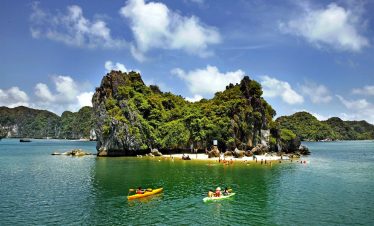 Stunning view of Halong Bay with kayakers exploring lush island scenery under bright blue sky.