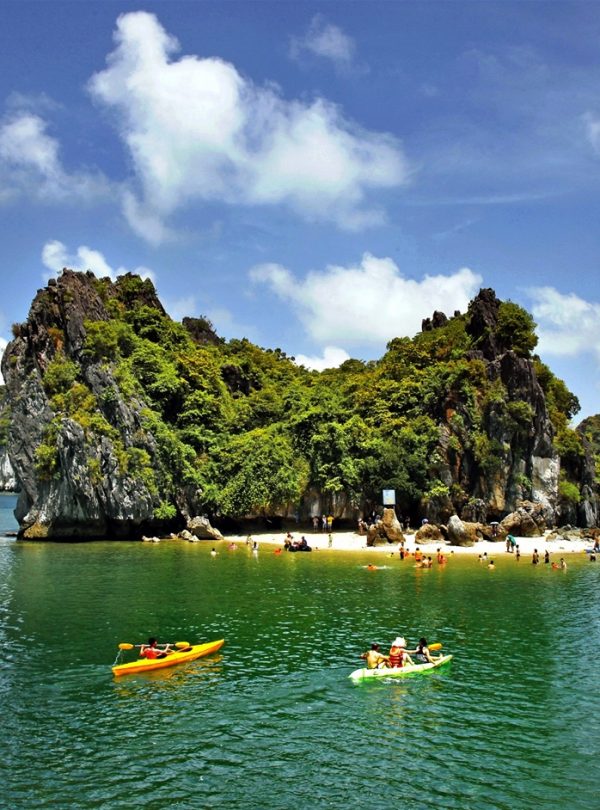 Stunning view of Halong Bay with kayakers exploring lush island scenery under bright blue sky.