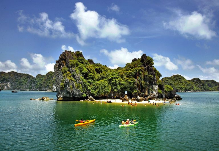 Stunning view of Halong Bay with kayakers exploring lush island scenery under bright blue sky.