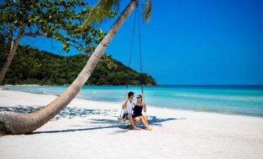 Relaxing beach scene with two women sitting under a palm tree on a pristine white sand beach in Viet.