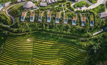 Aerial view of lush terraced rice paddies and traditional village homes in Sapa, showcasing Vietnam’.