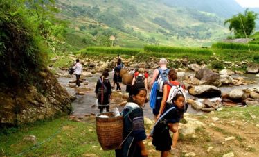 Vivid scene of travelers trekking along a river in Sapa with lush green mountains in the background.