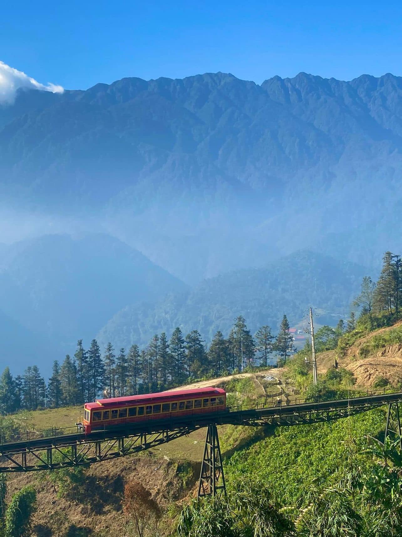 Scenic mountain train crossing lush green hills with towering peaks in Vietnam.