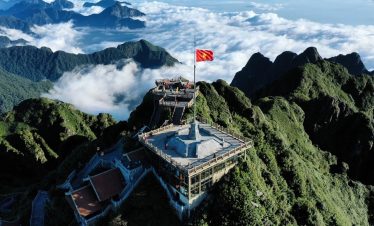 Breathtaking mountain landscape with lush green peaks and a flag atop a scenic viewpoint.
