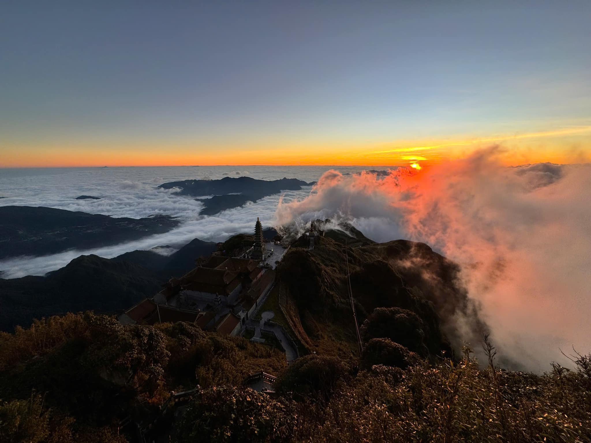 Majestic sunset view from Fansipan Mountain with clouds and rugged terrain, perfect for trekking and.