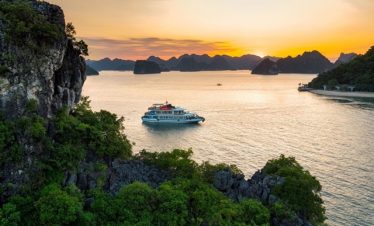 A scenic view of a luxury cruise sailing through Halong Bay's emerald waters at sunset.