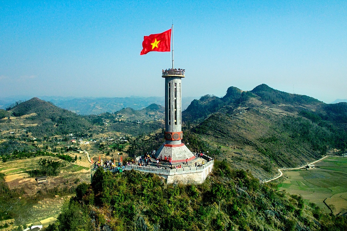 Vietnamese flag on a hilltop monument with scenic mountain views, symbolizing Vietnam's rich history.