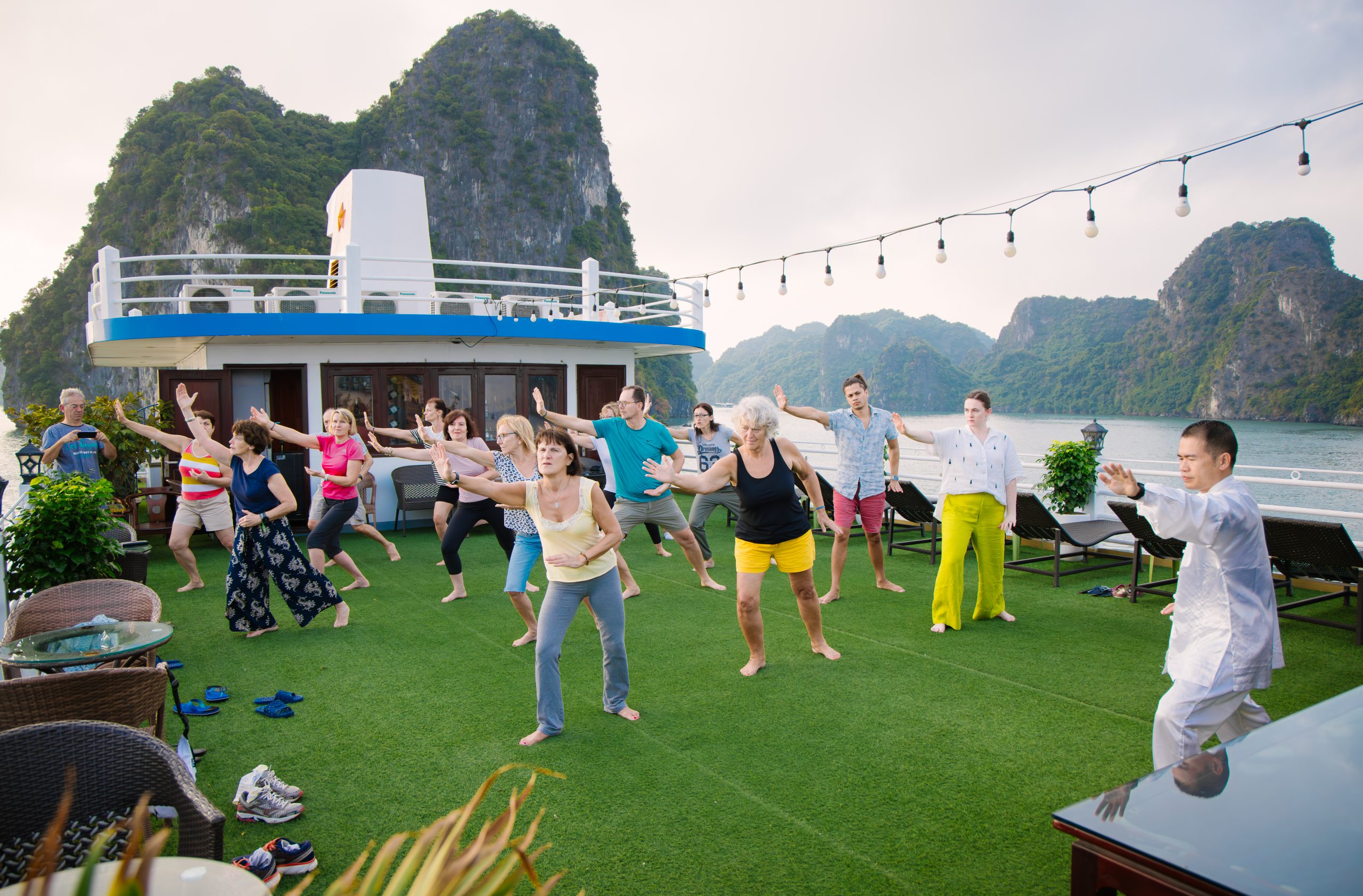 Vibrant scene of travelers dancing on a luxury cruise deck amidst stunning Halong Bay scenery.