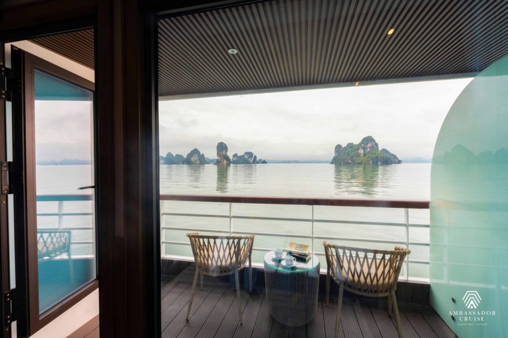 Scenic view of Halong Bay from a cruise balcony with two chairs and a table, showcasing tranquil wat.