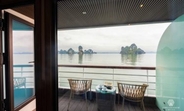Scenic view of Halong Bay from a cruise balcony with two chairs and a table, showcasing tranquil wat.