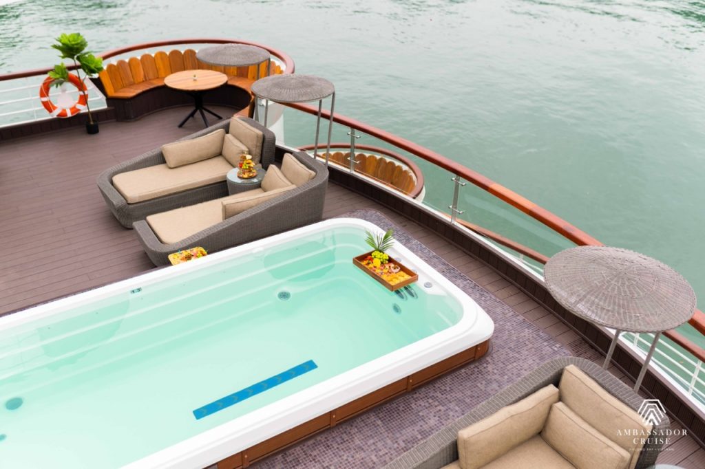 Relaxing cruise balcony with hot tub and lounge seating overlooking Halong Bay waters. Perfect for a.