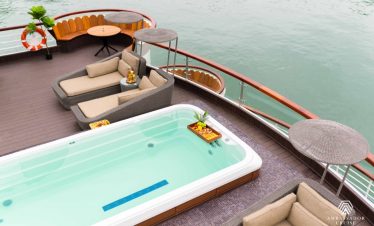 Relaxing cruise balcony with hot tub and lounge seating overlooking Halong Bay waters. Perfect for a.