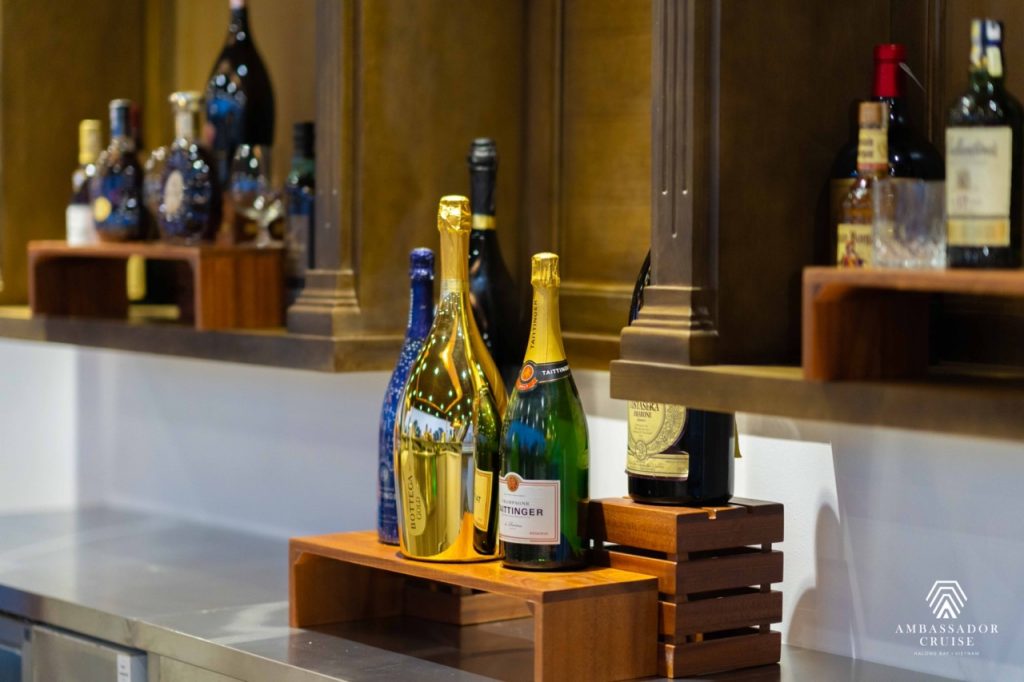 Luxurious bottles of champagne on cruise bar with elegant wooden shelves, Halong Bay scenery in back.