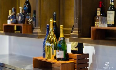 Luxurious bottles of champagne on cruise bar with elegant wooden shelves, Halong Bay scenery in back.