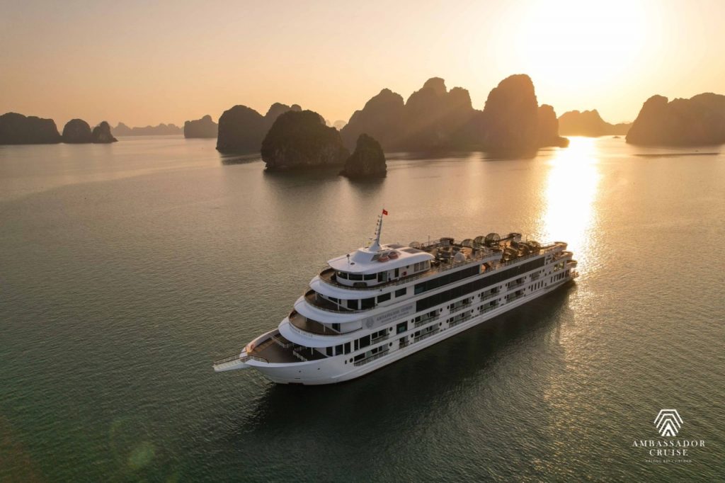 Elegant cruise ship sailing through Halong Bay at sunset, scenic limestone karsts and calm waters.
