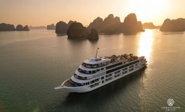 Elegant cruise ship sailing through Halong Bay at sunset, scenic limestone karsts and calm waters.