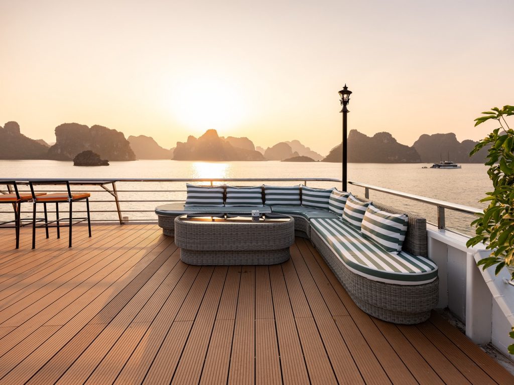 Stunning sunset view from a Halong Bay cruise balcony with seating, limestone karsts, and calm water.