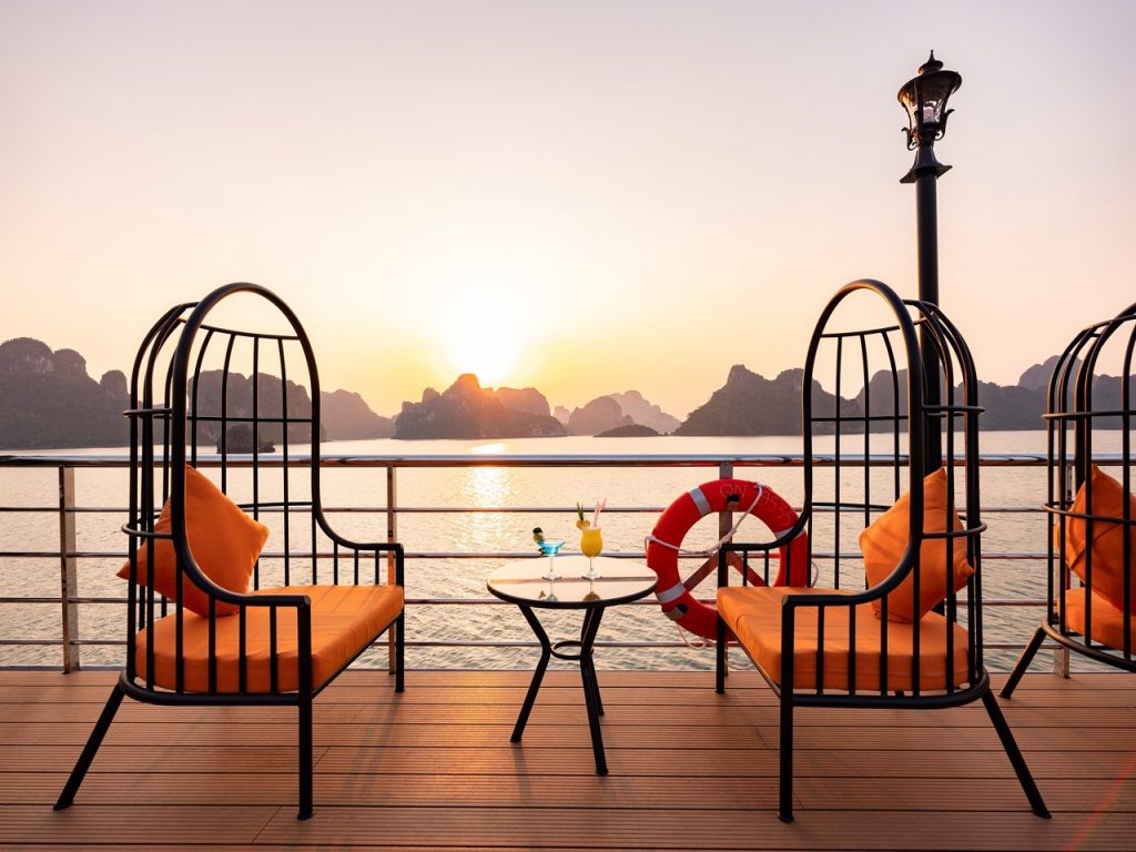 Scenic Halong Bay cruise balcony with sunset, comfortable chairs, and relaxing atmosphere.