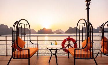 Scenic Halong Bay cruise balcony with sunset, comfortable chairs, and relaxing atmosphere.