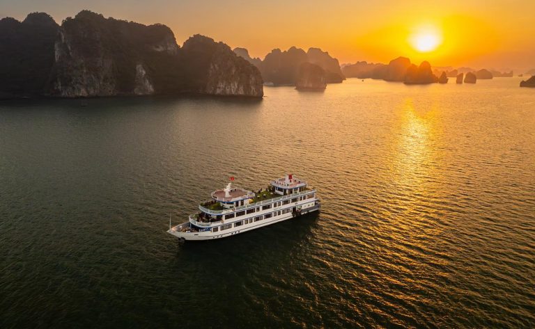 Sunset over Bai Tu Long Bay with luxury cruise sailing through scenic limestone islands.