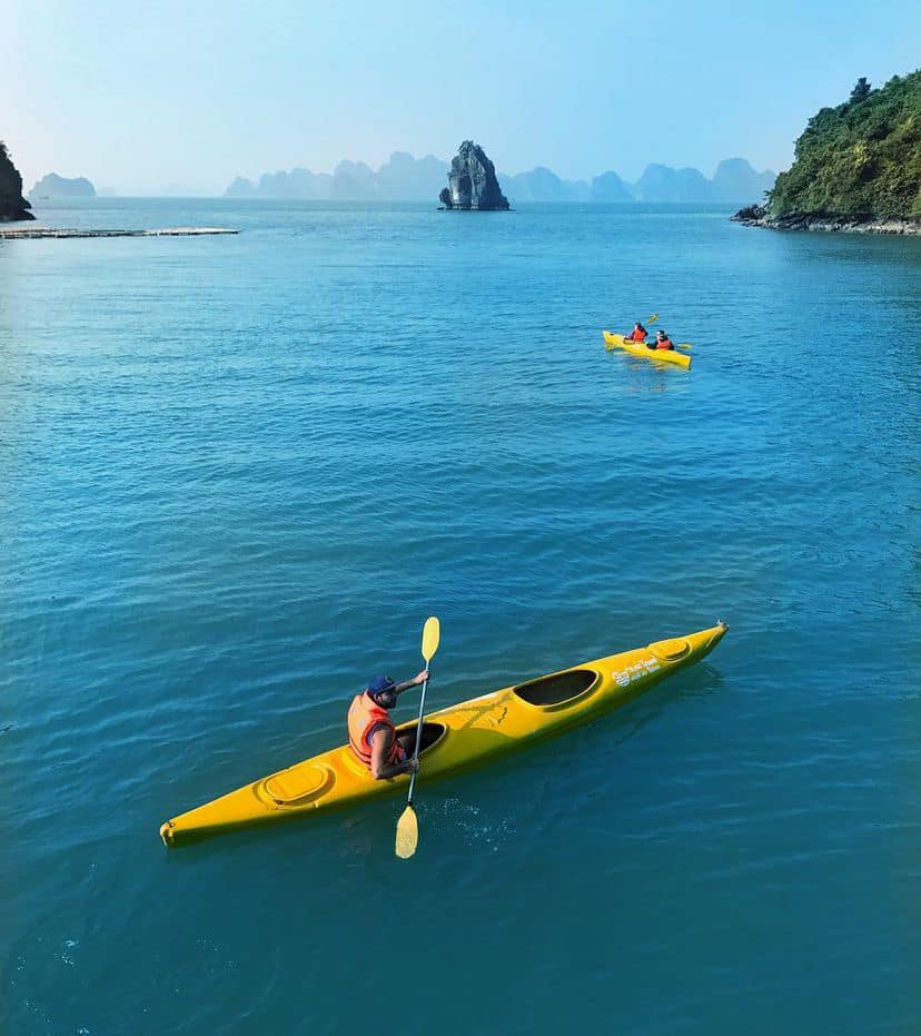 Kayaking scene in Halong Bay with vibrant yellow kayak and stunning limestone islands in the backgro.