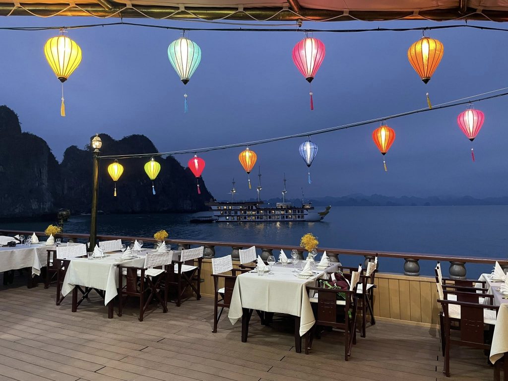 Scenic Bai Tu Long Bay with colorful lanterns, outdoor dining setup, and tranquil waters, perfect fo.
