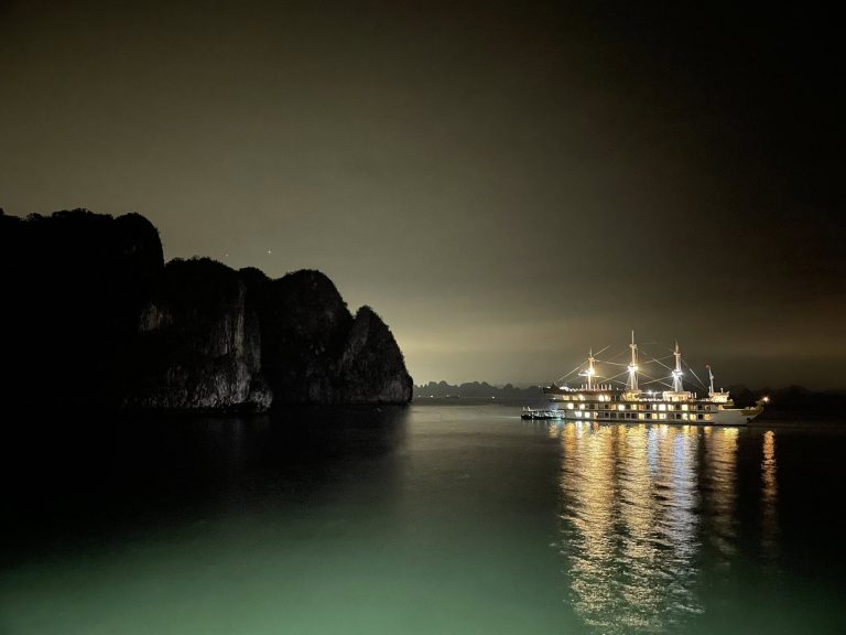 Bai Tu Long Cruise 2 Nights - view of Bai Tu Long Bay with illuminated cruise ship reflecting on calm waters, surrounded by.