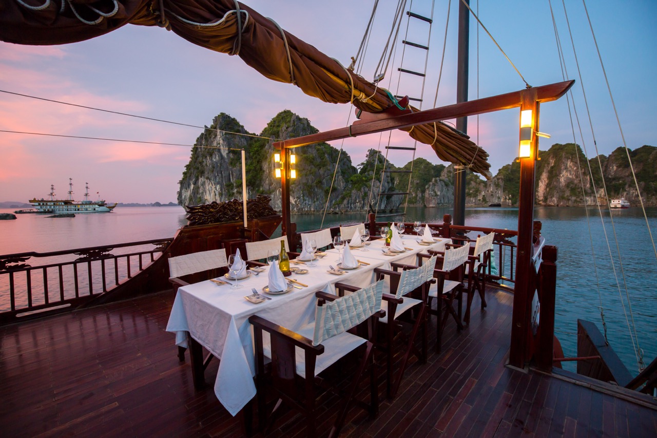 Elegant dining on Bai Tu Long Bay cruise balcony with stunning sea views and sunset ambiance.