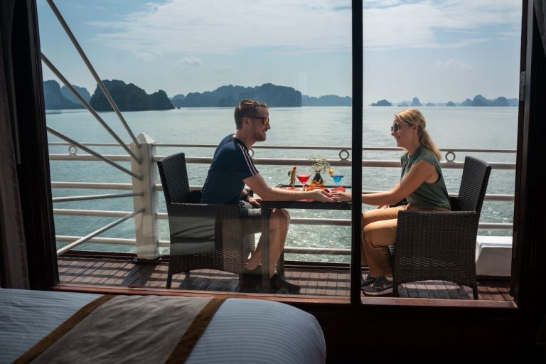 Couple enjoying dinner on a cruise balcony with stunning views of Halong Bay's limestone karsts and.