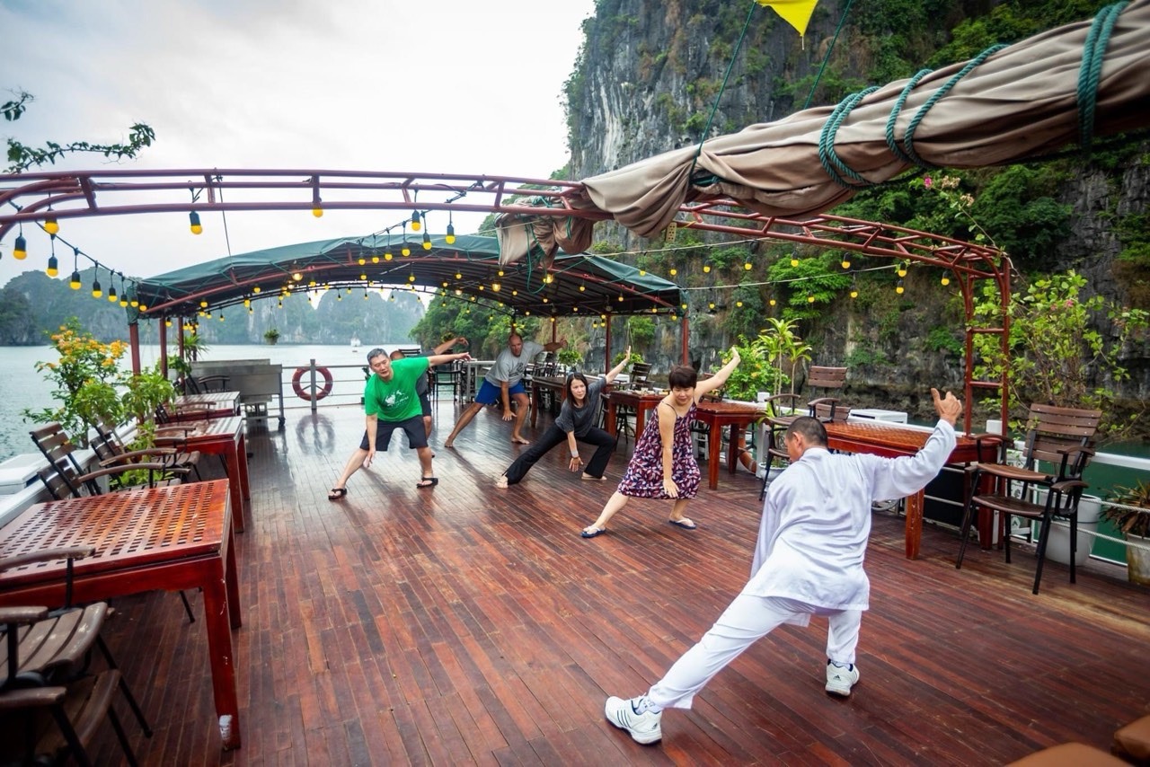 Relaxing Tai Chi session on Bai Tu Long Bay cruise deck at sunrise.