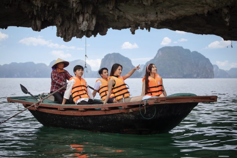 Vivid scene of tourists kayaking under a limestone cave in Halong Bay, showcasing stunning seascape.
