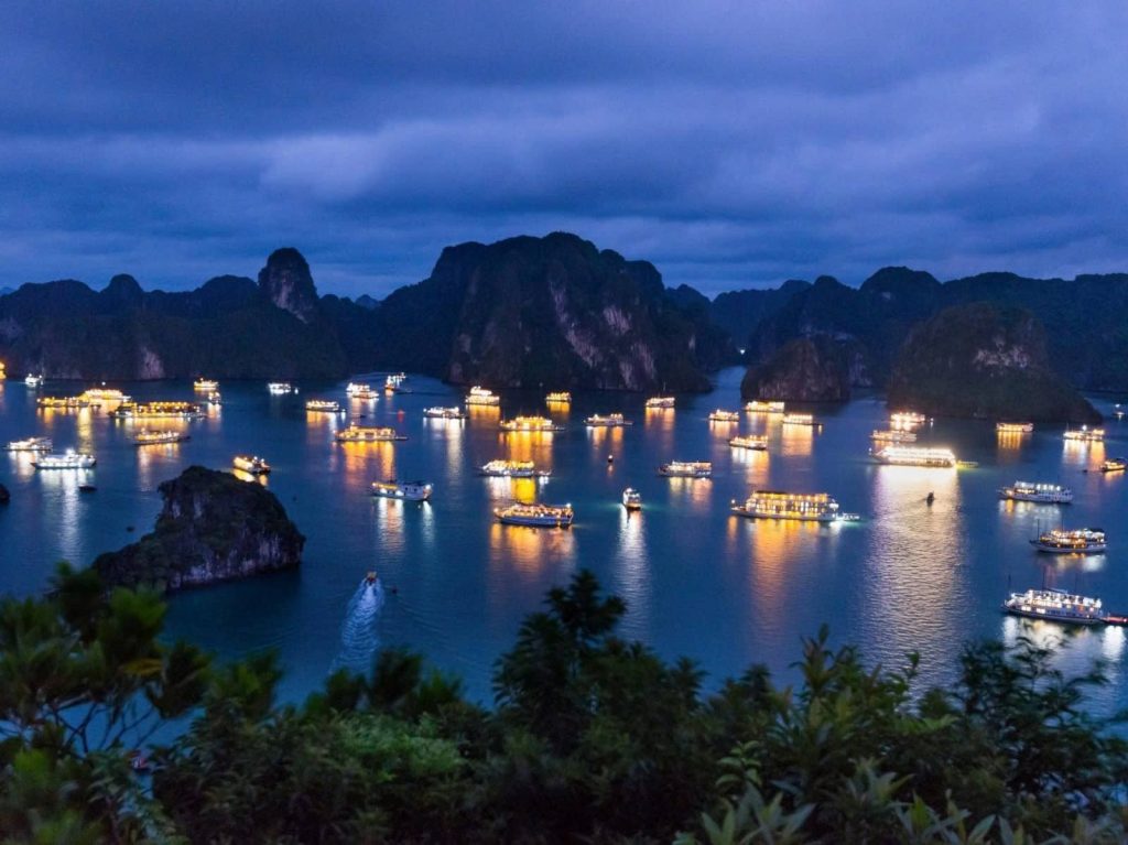 Stunning night scene of Halong Bay with illuminated boats and dramatic limestone karsts under a mood.