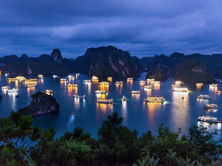 Stunning night scene of Halong Bay with illuminated boats and dramatic limestone karsts under a mood.