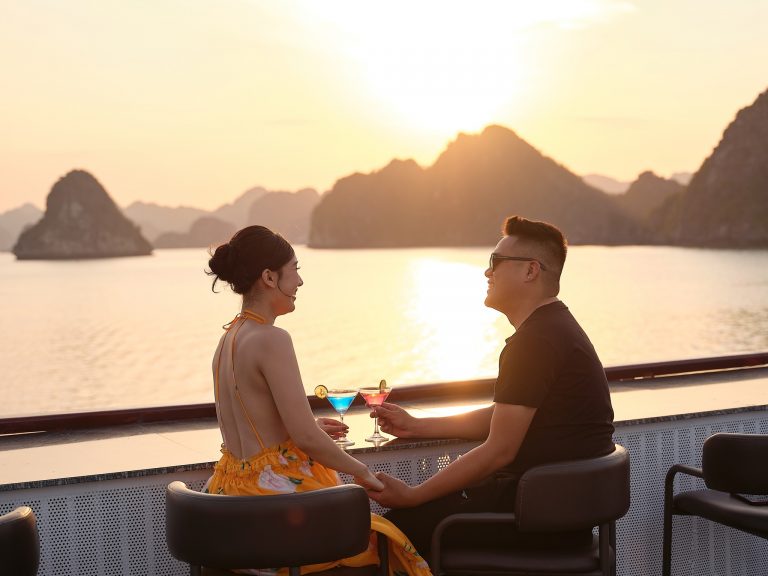 Halong Bay cruise balcony with couple enjoying sunset view, romantic travel experience.