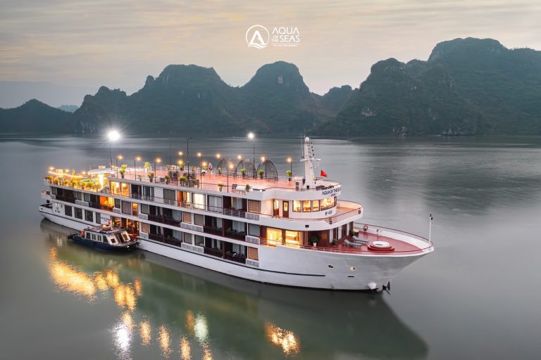 Lan Ha Bay Cruise 2 Nights - Luxury Halong Bay cruise at sunset with illuminated decks and scenic mountain backdrop.