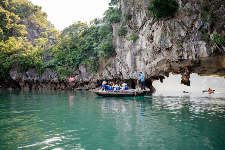 Scenic view of a boat passing through a limestone cave in Halong Bay with lush greenery.