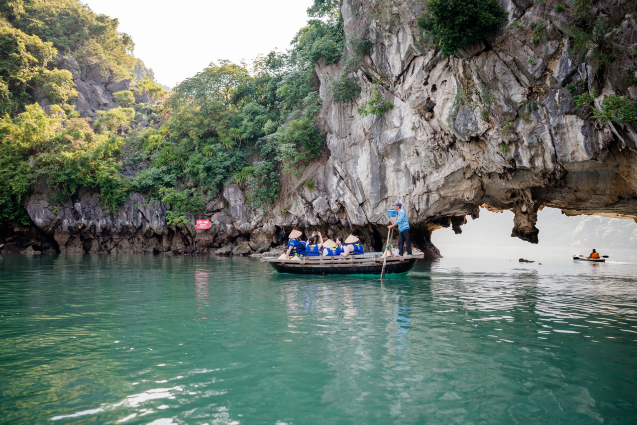 Scenic view of a boat passing through a limestone cave in Halong Bay with lush greenery.