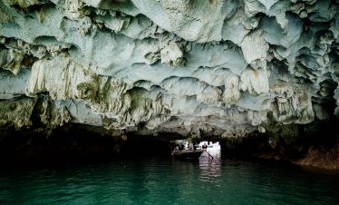 Cave interior in Halong Bay with boat passing underneath, scenic and adventurous atmosphere.
