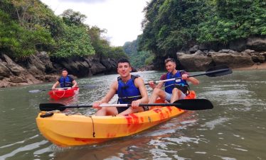 Kayakers paddling through calm waters of Halong Bay, surrounded by lush green cliffs, enjoying a sce.