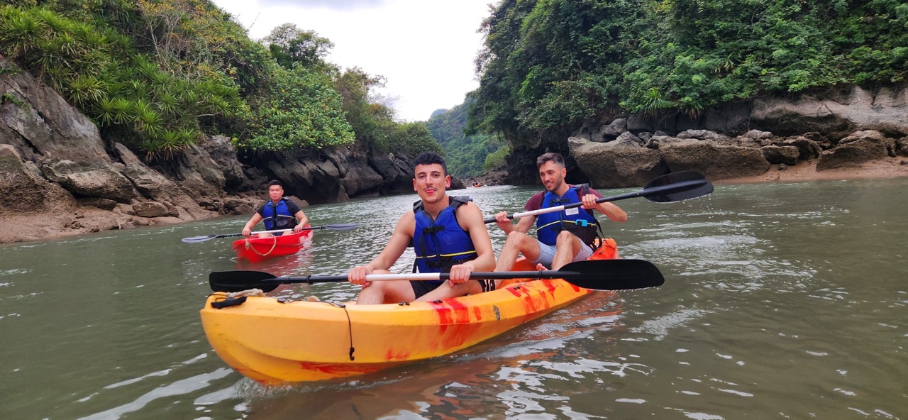 Kayakers paddling through calm waters of Halong Bay, surrounded by lush green cliffs, enjoying a sce.