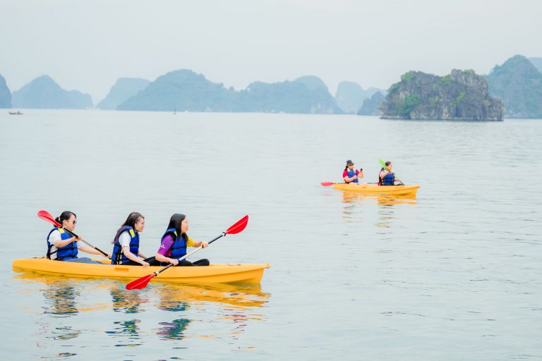 Kayakers paddling on calm Halong Bay waters with limestone islands in the background.