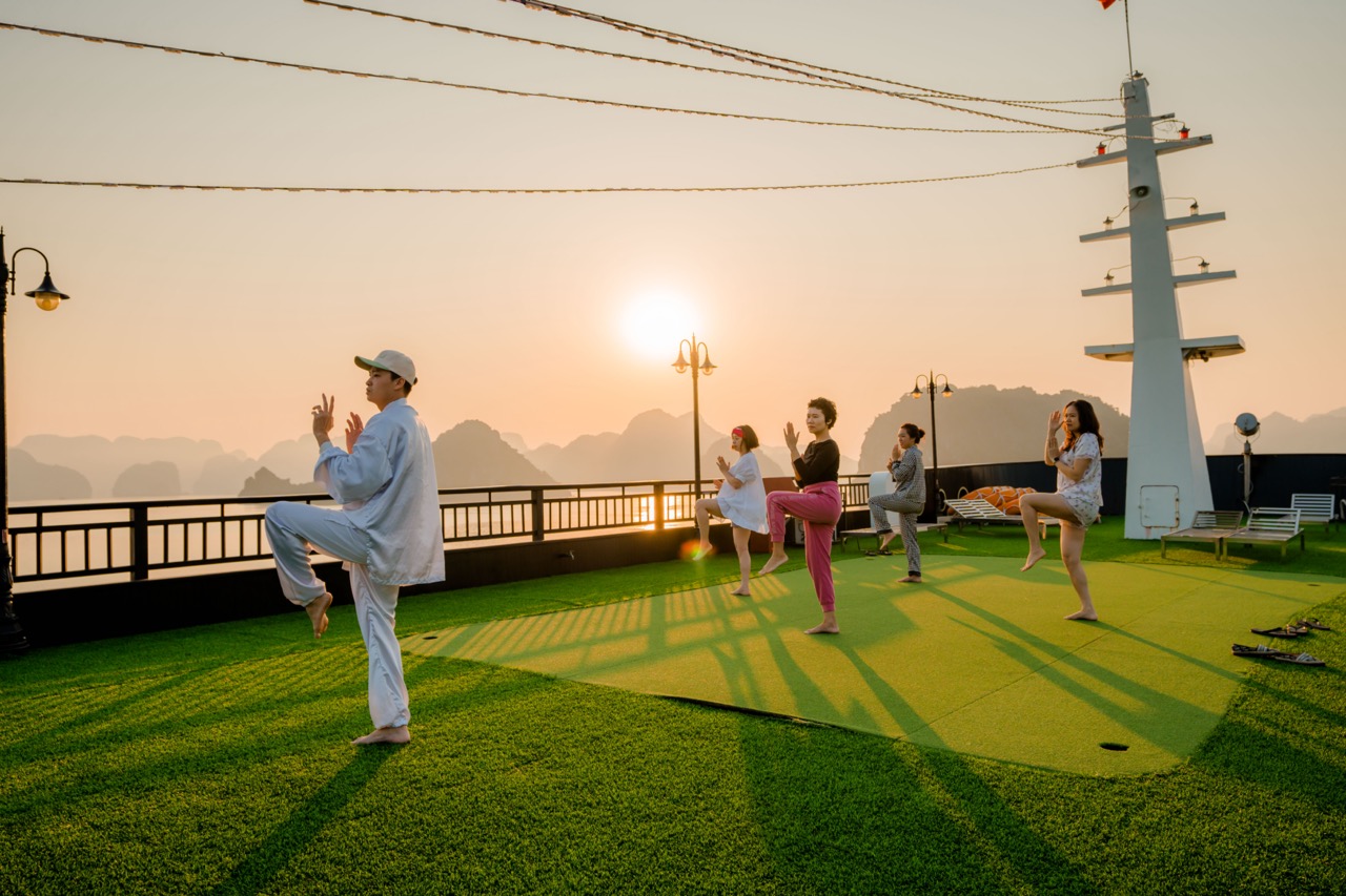 Sunset yoga on cruise deck with people practicing yoga and meditation in Halong Bay at sunset, peace.