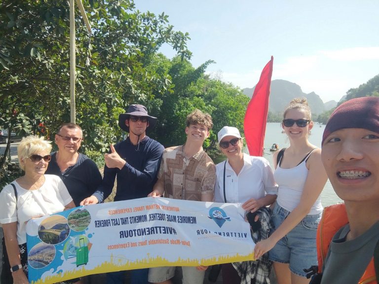 Scenic group photo of travelers holding a ViettrendTour banner outdoors in lush green surroundings.