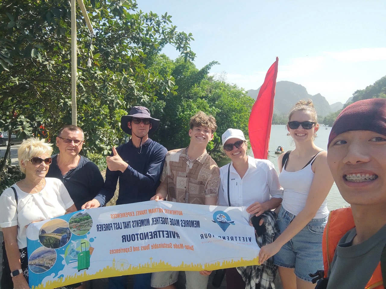 Scenic group photo of travelers holding a ViettrendTour banner outdoors in lush green surroundings.