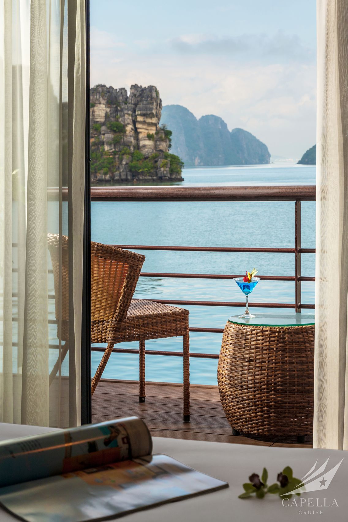 Stunning ocean view from a hotel balcony with wicker furniture and a blue cocktail.