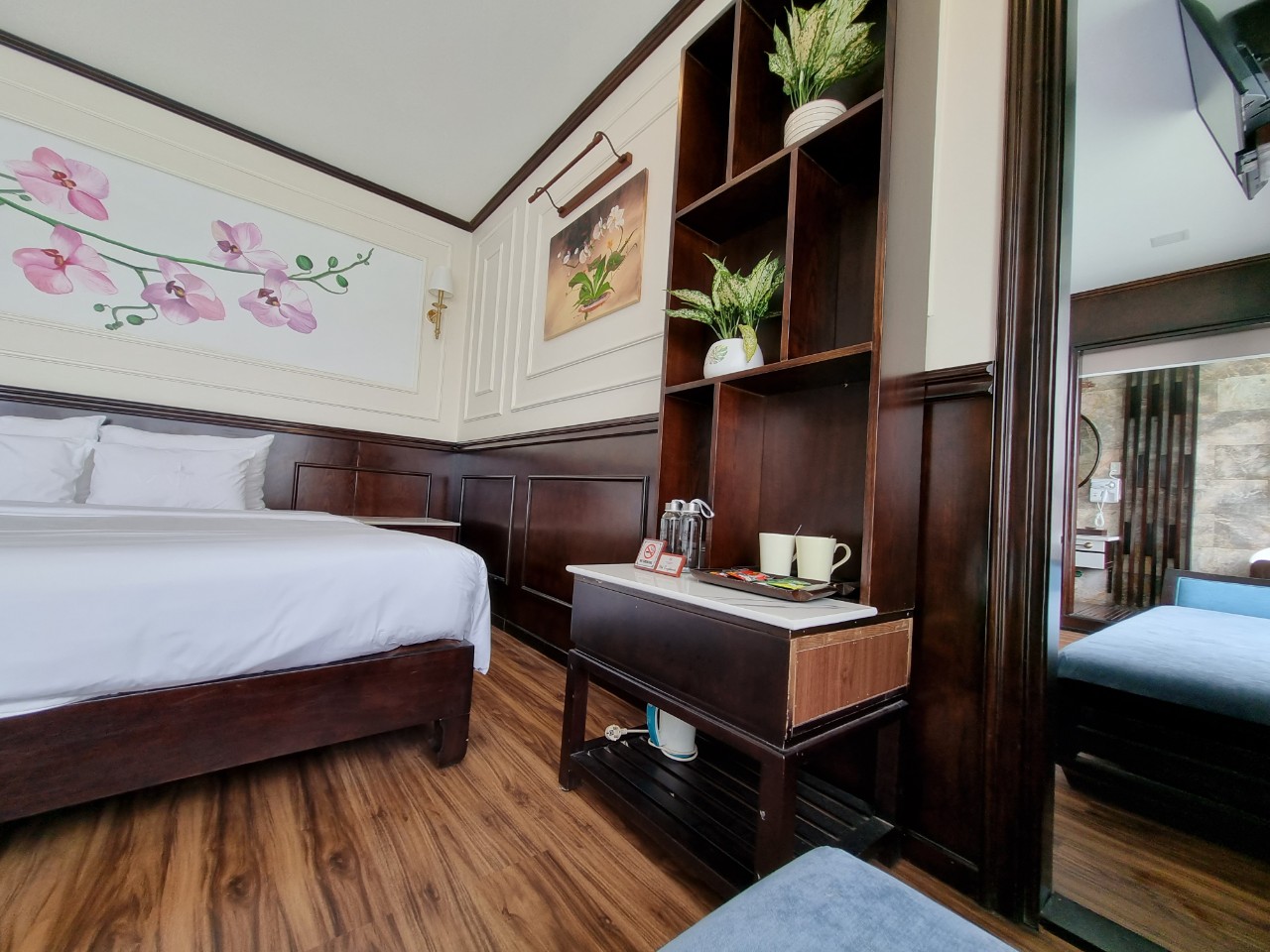Comfortable hotel bedroom with wooden furniture, floral wall art, and cozy ambiance.