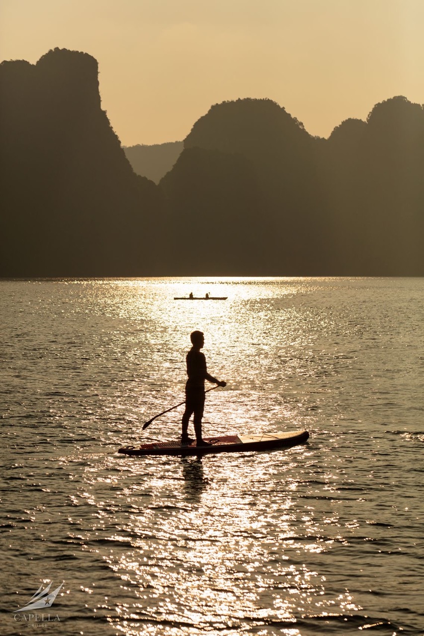 1. Person paddleboarding on a tranquil river at sunset with mountainous backdrop.